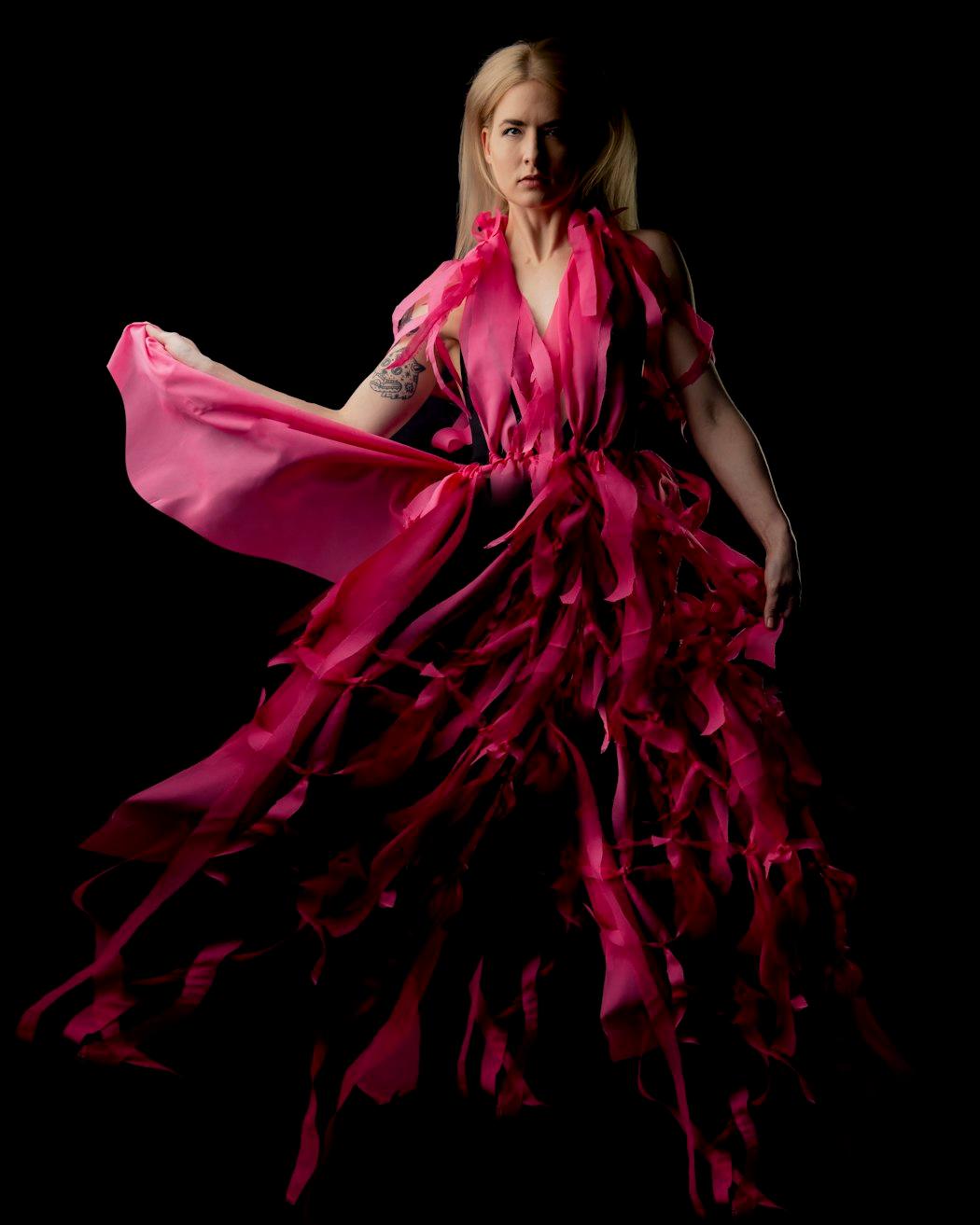 Woman wearing a dramatic pink dress against a black studio background