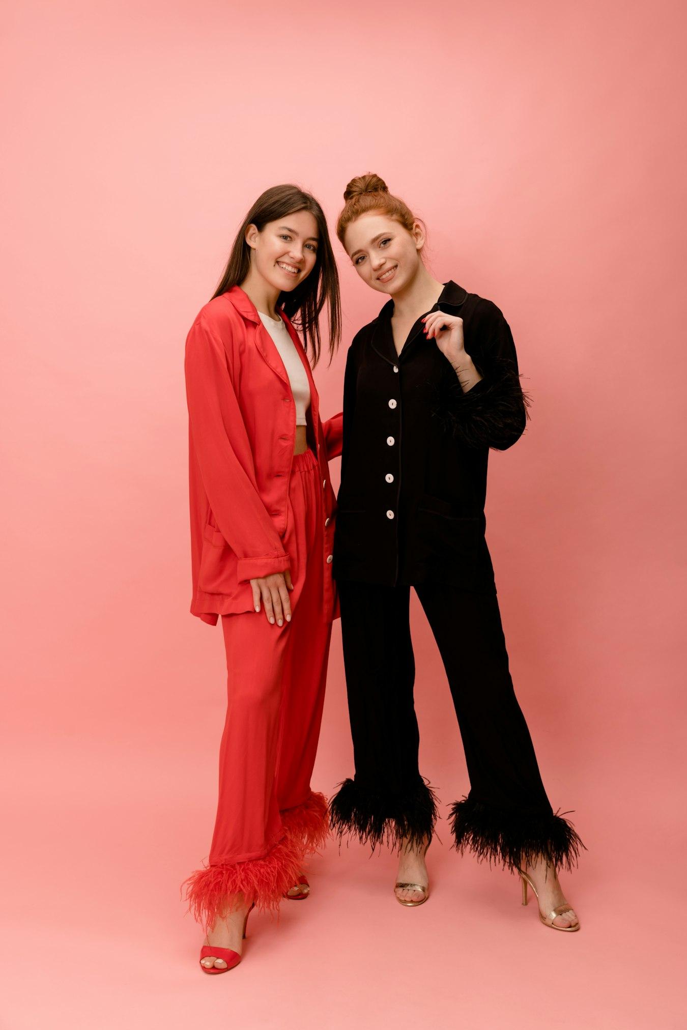 Two women in expressive red and black looks in a pink studio